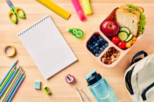 istock Empty notebook, lunchbox with fruit, vegetables, nuts, school supplies on wooden table. Top view. Kids lunch box for school dinner. 1567410367