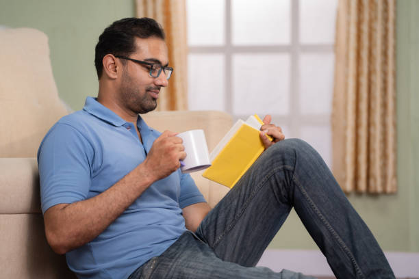 istock handheld shot of Indian man reading book by drinking coffee or tea while sitting on floor at home - concept of refreshment, knowledge and weekend hobbies 1567411485