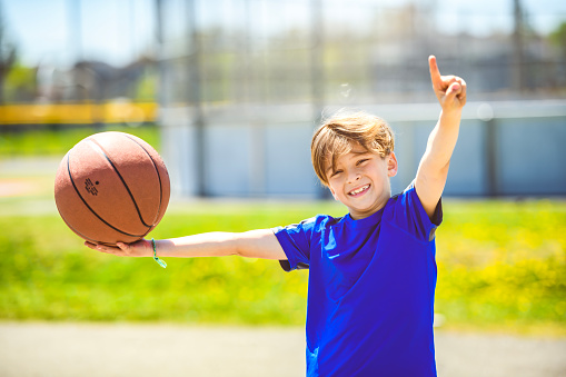 A portrait of a kid boy playing with a basketball in park