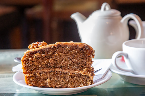 A close up of a slice of cake, with a teapot and cup and saucer behind