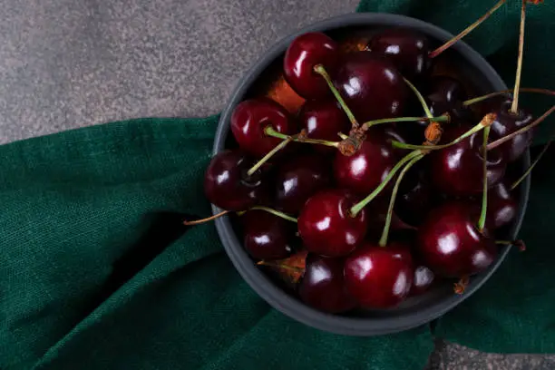 Photo of Black cherries on a gray plate on green cloth