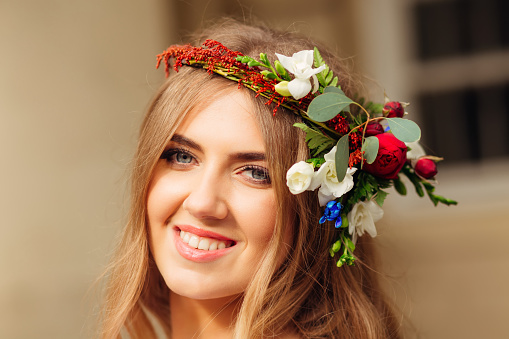 Gorgeous ukrainian girl looking at camera with a crown of fresh flowers on her head. Smiling young woman with blond long hair