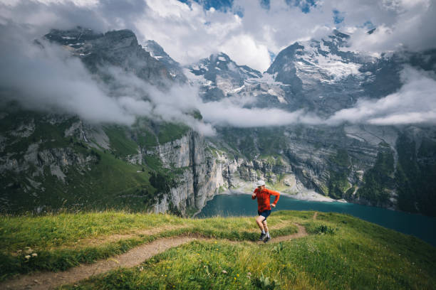 Active mountain trail runner dressed bright t-shirt with a backpack in sports sunglasses running endurance ultramarathon race by picturesque hills at sunset time. Sporty active people concept image.