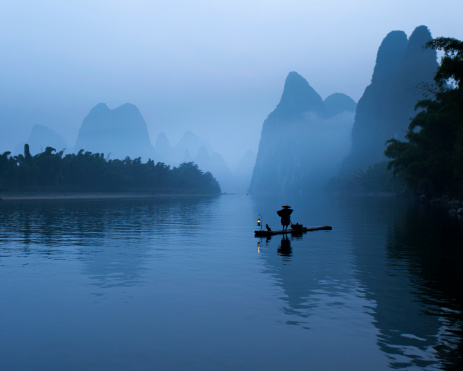 Cormorant fisherman rafts down the Li River in mysterious morning light near Xingping Town, Guangxi province, China.