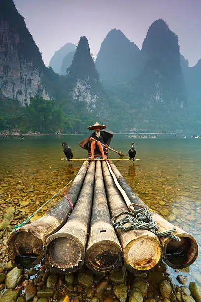 Cormorant fisherman sits on his bamboo raft on the banks of the Li River near the village of Xingping, Guangxi region, China.
