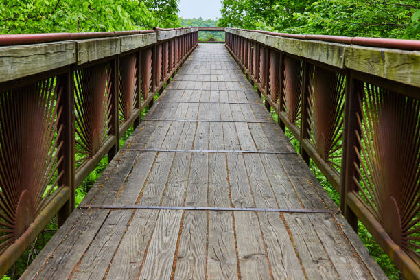 istock Long view of bridge with worn planks and rusty rising sun pattern on railing bars 1567431280