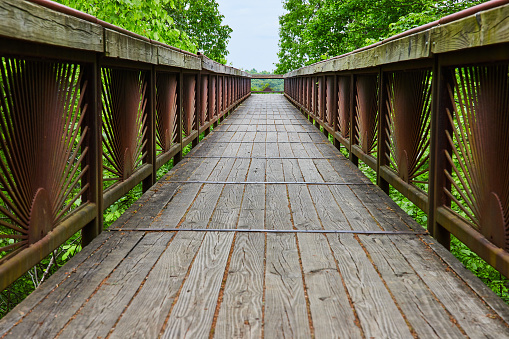 Image of Low angle of bridge with setting sun pattern on railing and wooden walkway path over tree tops