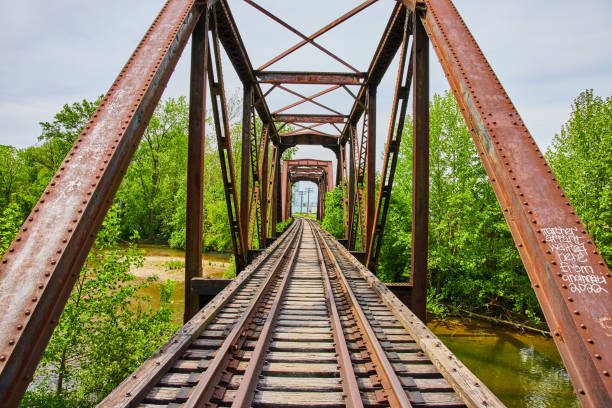 istock Old railroad bridge with train tracks cutting through trees leading to city 1567441787