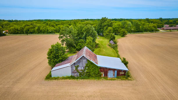 istock Old rusty barn in center with empty dirt farmland on three sides and a lush green forest behind aerial 1567441789