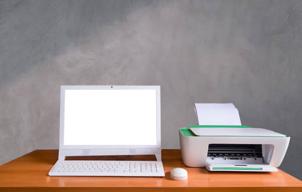 istock White computer with wireless keyboard and printer on wooden desk in front of gray concrete loft wall background, blank screen with clipping path 1567460344