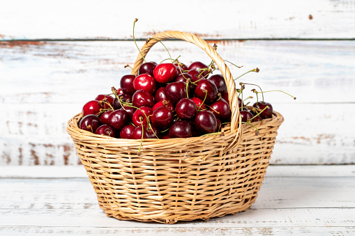 Fresh cherry in a wicker basket over wooden background. Cherry harvest season concept. Healthy and fresh fruit