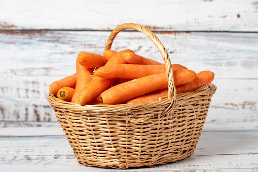 Fresh carrots in a wicker basket over wooden background. Carrot harvest season concept. Vegetables for a healthy diet