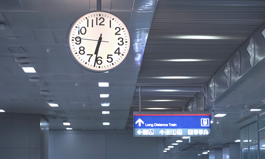 One single backlit clock on a darkened train station platform, public area object closeup detail. Commute transportation rush hour, haste and hurry, passage of time abstract concept, dark shot, nobody