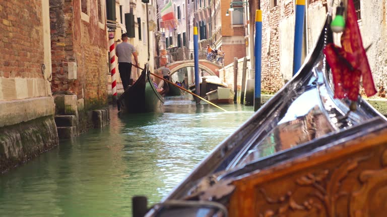 View from the front of the gondola of Venice canals, architecture of the city and other gondolas  during ride along the canals in Venice, Italy.