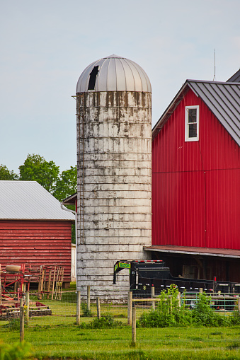 Image of Vertical of dirty white silo outside pristine red barn