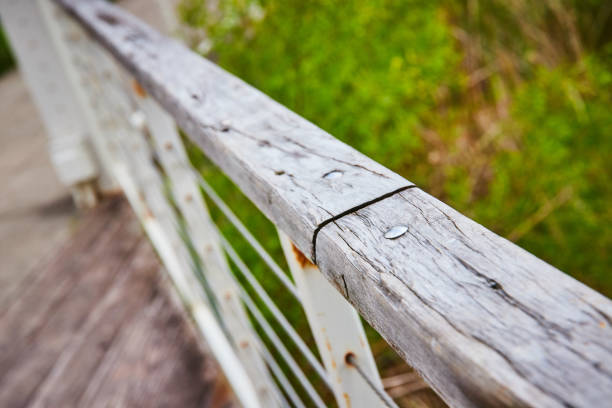 Image of Weathered wooden railing atop rusty white railing macro close up with path and blurry grass