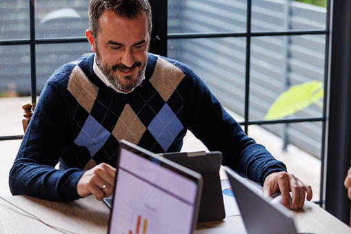 Portrait of mid adult businessman sitting at his desk and reviewing data on laptop.