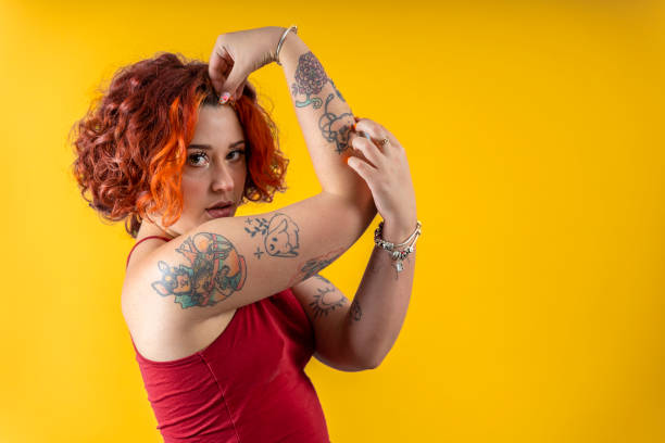 lgbtのノンバイナリーの女性。自由を表現する:黄色の背景にタトゥーを入れたジェンダークィアの人 - anti sex ストックフォトと画像