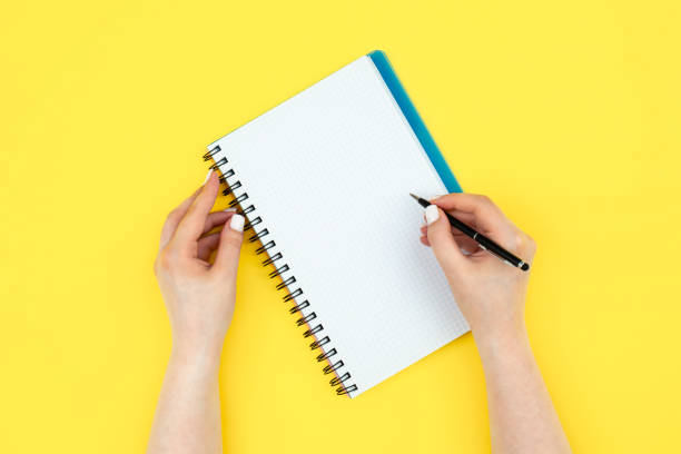 istock Female hands writing in notepad on yellow background, flat lay. 1567520562