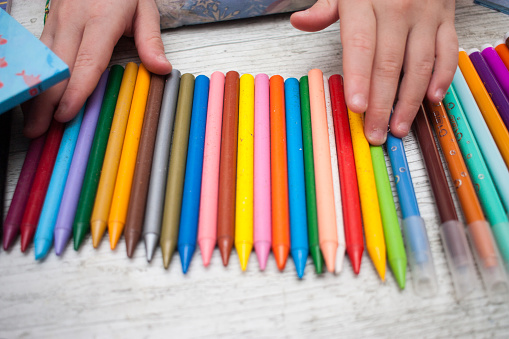 child hands with colored crayons on light colored table