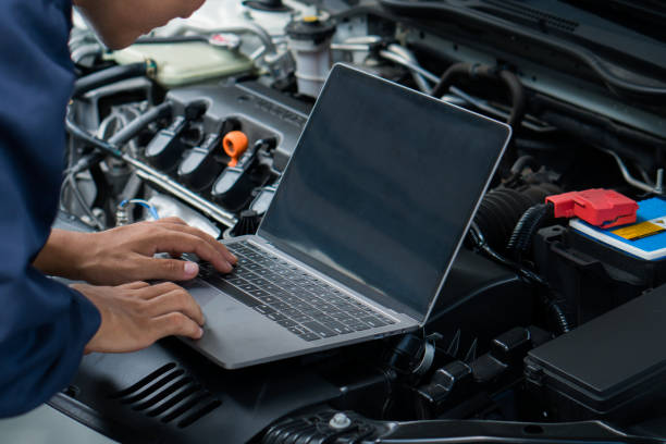 istock Car mechanic using laptop computer examining tuning fixing repairing car engine in garage.Car repair service and maintenanc concept. 1567587320