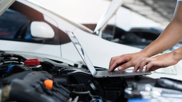 istock Car mechanic using laptop computer examining tuning fixing repairing car engine in garage.Car repair service and maintenanc concept. 1567587860