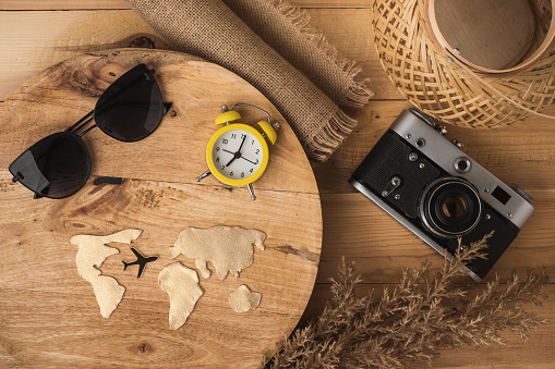 Top view of tourist essentials: Retro camera, sunglasses, passport next to golden world map and airplane silhouette on wooden background. Travel concept background with travelers accessories. Flat lay