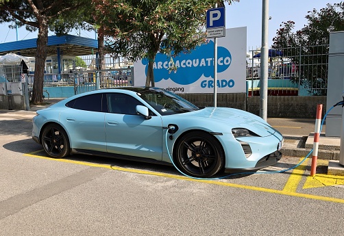 Grado, Italy. July 23, 2023. Blue Porsche Taycan Turbo S on charging at the roadside. It is a battery electric car of the  luxury german automaker.