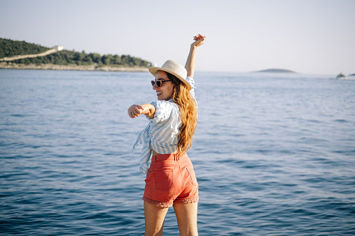 Back side view of happy woman with hat on beach and hand up