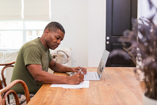 During his leave from the military, the mid adult male soldier works on a continuing education course in his dining room.