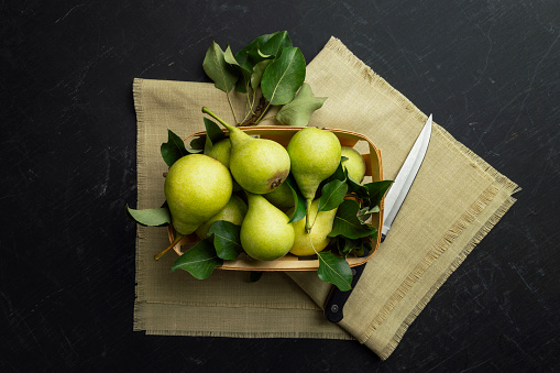Gardening. Autumn harvest. Green ripe pears in a box on a dark background. pear from the garden. Delicious pears close-up. Top view, flat lay. Copyspace. Banner.