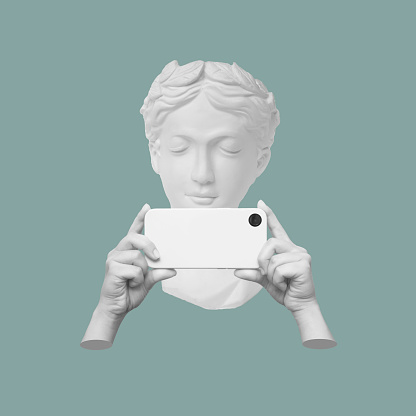 Antique statue's head holding mobile phone with photo camera in the hands taking picture on sage green color background. 3d trendy creative collage in magazine style. Contemporary art. Modern design