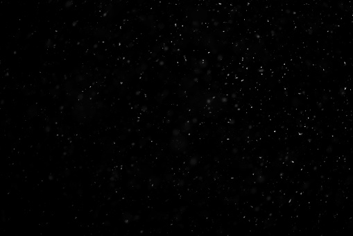 Close up white snow falling over black background of night winter sky in the dark