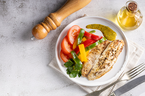 Grilled tilapia fillet with spices and colored peppers.