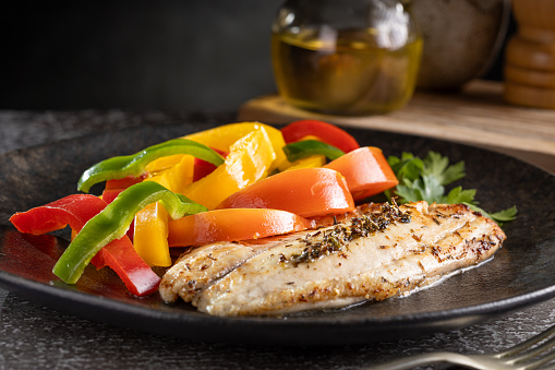 Grilled tilapia fillet with spices and colored peppers.