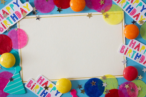 A blank party invitation with copy space, surrounded by happy birthday confetti, candy and stars .