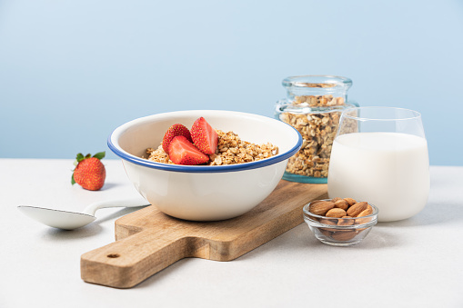 Granola in bowl with strawberries on blue background with copy space
