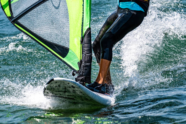Young man jumping on waves with colourful windsurfing board and sail.