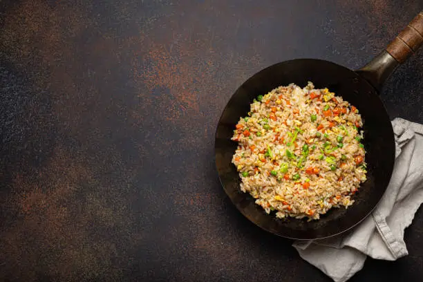 Photo of Authentic Chinese and Asian fried rice with egg and vegetables in wok top view on rustic concrete table background. Traditional dish of China with space for text
