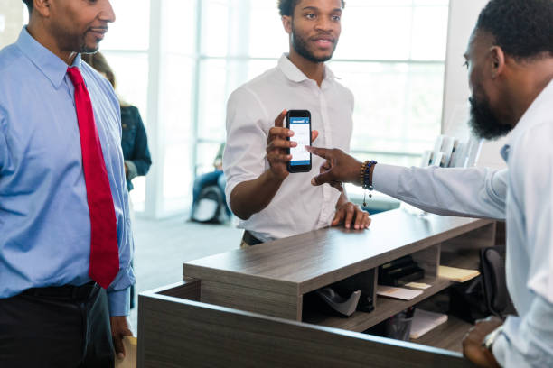 istock Bank teller helps young man with mobile banking app 1567851928