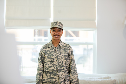 The proud young adult female soldier poses for a photo in the living room of her home.