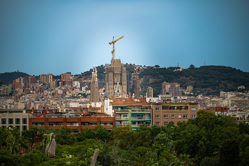 Barcelona, Spain - May 25 2022: View of the mountains, treetops, rooftops and the construction of the Sagrada Familia in Barcelona.