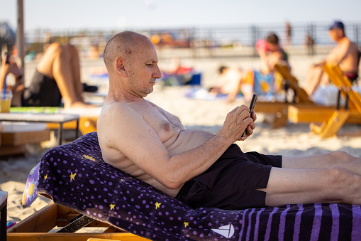 A man reclining on a beach chair, enjoying his phone amidst the tranquil surroundings.