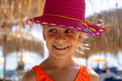 A cute little girl wearing a red hat happily explores the sandy beach.
