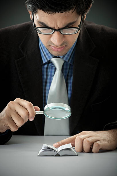 uomo d'affari alla ricerca di un libro attraverso la lente di ingrandimento in miniatura - suit necktie close up gray foto e immagini stock