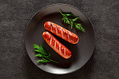 Grilled sausages on plate with dill sprigs, on dark background, top view