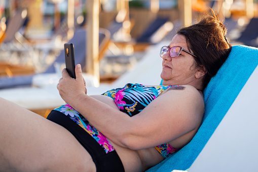 A woman in complete relaxation mode, phone in hand, by the beach.