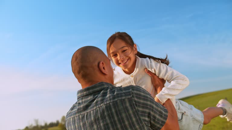 SLO MO Father spinning his daughter in the sunny meadow and smiling