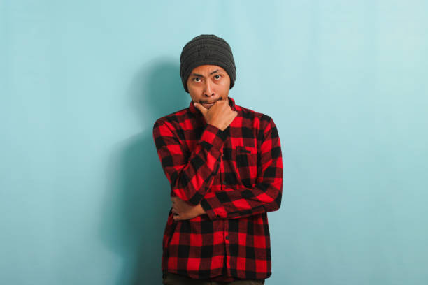 istock Thoughtful Young Asian man holds his chin, making plans, isolated on a blue background 1567927375