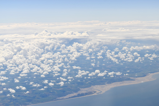 Viewed from high altitude throughout white clouds floating above green land and coast.